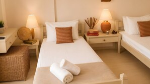 Ein Hotelzimmer mit zwei Betten, Nachttischen, Lampen, einer kleinen Pflanze und einer gewebten Matte.