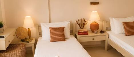 A hotel room with two beds, bedside tables, lamps, a small plant, and a woven mat.
