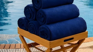 A wooden stand with rolled blue towels by a pool.