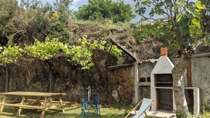 Eine ländliche Außenansicht mit einem Holztisch, einem blauen Klappstuhl und einem kleinen Gebäude mit Schornstein.