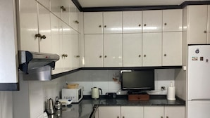 Eine Küche mit weißen Schränken, einer Mikrowelle, einem Wasserkocher, einem Toaster, einem Kühlschrank und einem Fernseher.
