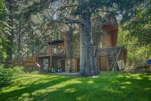 Eine Holzhütte mit Steinaußenwand, einer Holzterrasse und einem großen Baum davor.
