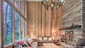Een gezellige woonkamer met een houten wand, een open haard en een groot raam met uitzicht op groen.