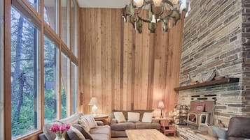 A cozy living room with a wooden wall, a fireplace, and a large window overlooking greenery.