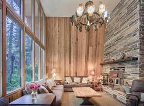 Ein gemütliches Wohnzimmer mit einer Holzwand, einem Kamin und einem großen Fenster mit Blick auf Grünflächen.