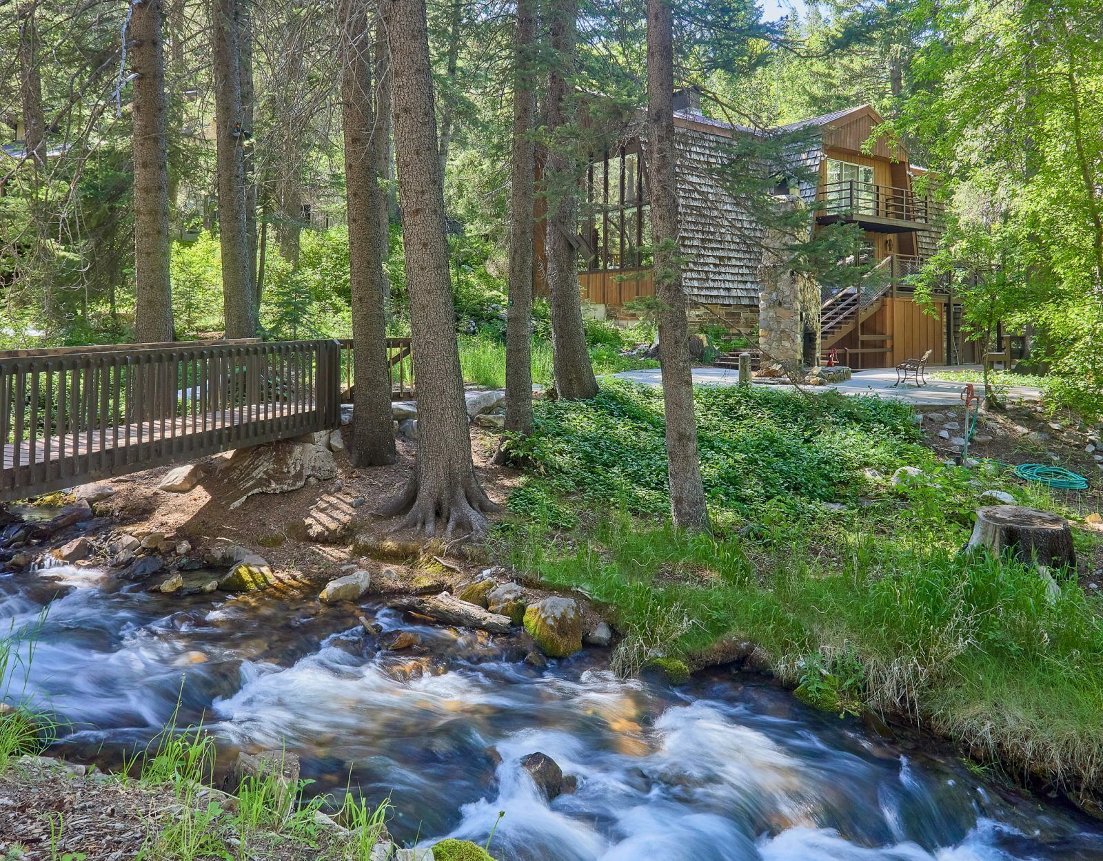 A wooden cabin with a stone foundation, surrounded by a forest and a flowing stream.