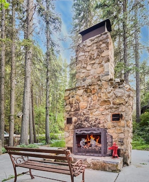 Ein Steinkamin mit Feuer, umgeben von einer Bank und Bäumen.