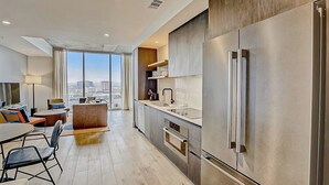 A modern kitchen with a large refrigerator, a dining area with a table and chairs, and a view of the city through large windows. - Austin Rainey Street condo w/private  balcony, rooftop pool & gym (Austin)