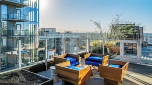 Eine Dachterrasse mit Glaswänden, Sitzmöglichkeiten im Freien und Blick auf die Stadtlandschaft.