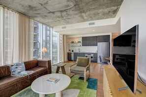 Ein modernes Wohnzimmer mit einer Couch, einem runden Tisch, einem Fernseher und einer Küche im Hintergrund.