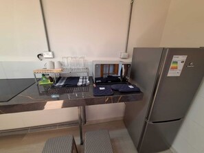 Una cocina compacta con un refrigerador de acero inoxidable, una encimera con cristalería y una cafetera.