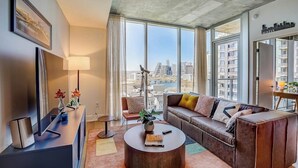 A modern living room with a sofa, coffee table, and a city view through large windows. - Austin Rainey Street perch with balcony - rooftop pool & gym (Austin)