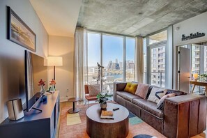 Ein modernes Wohnzimmer mit einer Couch, einem Couchtisch und Blick auf die Stadt durch große Fenster.