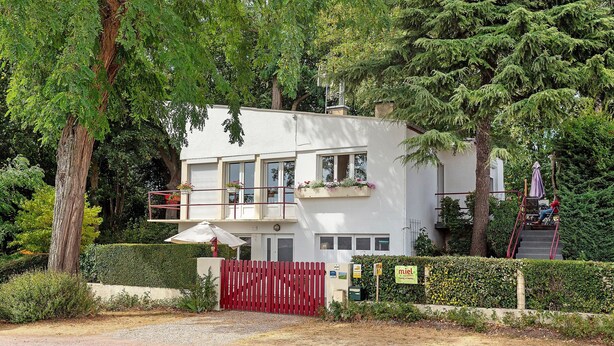 Un edificio moderno de dos pisos con fachada blanca, varias ventanas y una puerta roja.