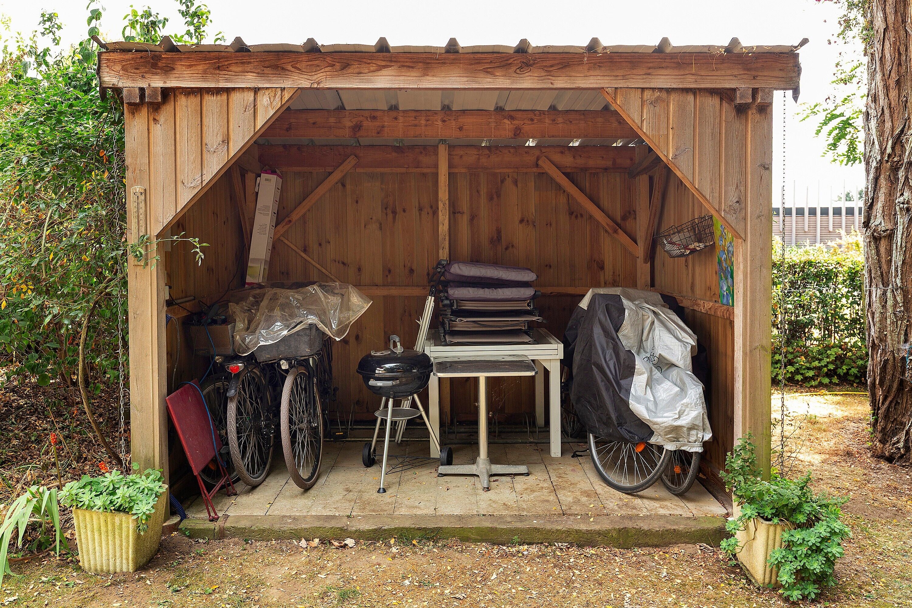 A wooden shed with a table, a covered grill, and a bicycle inside.