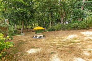 Un jardín con una mesa de picnic y sillas, rodeado de árboles y un cobertizo pequeño.