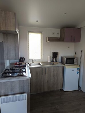 Eine kleine Küche mit einem Gaskochfeld, einer Mikrowelle, einem Spülbecken und einem kleinen Kühlschrank.