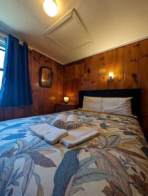 Ein Zimmer mit Holzwänden, einem Bett, einem Nachttisch und einer Wandleuchte.