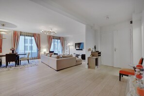 A spacious living area with a sofa, dining table, and chairs, a kitchen area, and a TV mounted on the wall. - TOP OF THE RANGE- LUXURY DESIGNER APARTMENT AVE RAYMOND POINACARE (Paris)