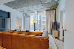 Ein modernes Wohnzimmer mit einer Couch, einem Fernseher und einem großen Fenster mit Vorhängen.
