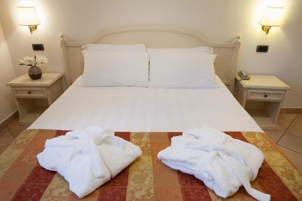 Une chambre d’hôtel avec un grand lit, deux tables de chevet, une petite table et deux peignoirs blancs posés sur le lit.
