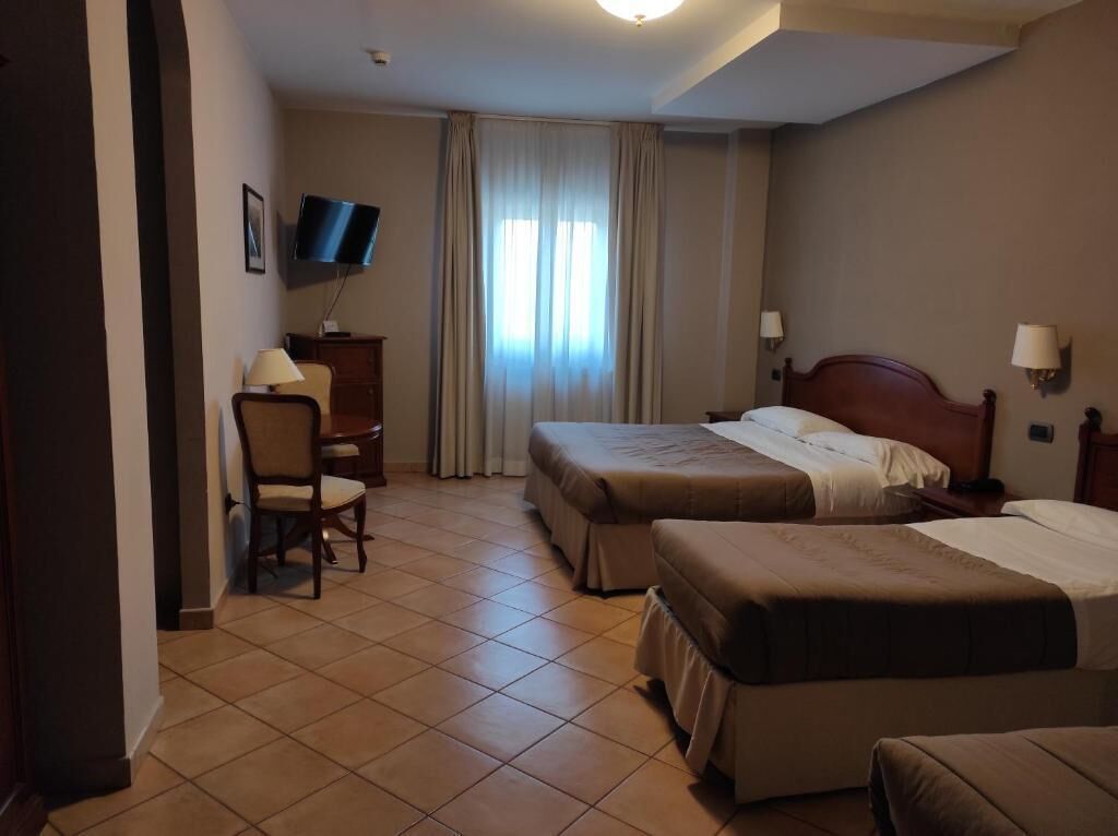 Habitación de hotel con dos camas, un escritorio, una silla, un televisor y una ventana con cortinas.