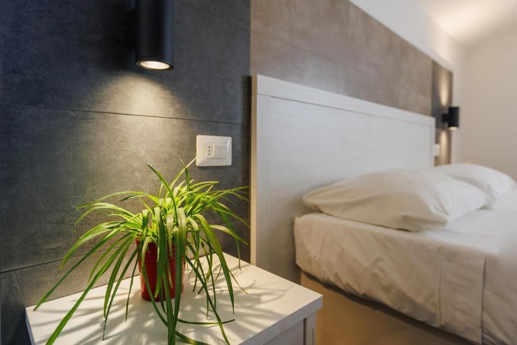 A modern bedroom with a bed, a bedside table with a plant, and a wall-mounted light fixture.