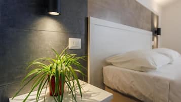 Una camera da letto moderna con un letto, un comodino con una pianta e un punto luce a parete.