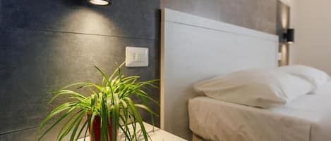 A modern bedroom with a bed, a bedside table with a plant, and a wall-mounted light fixture.
