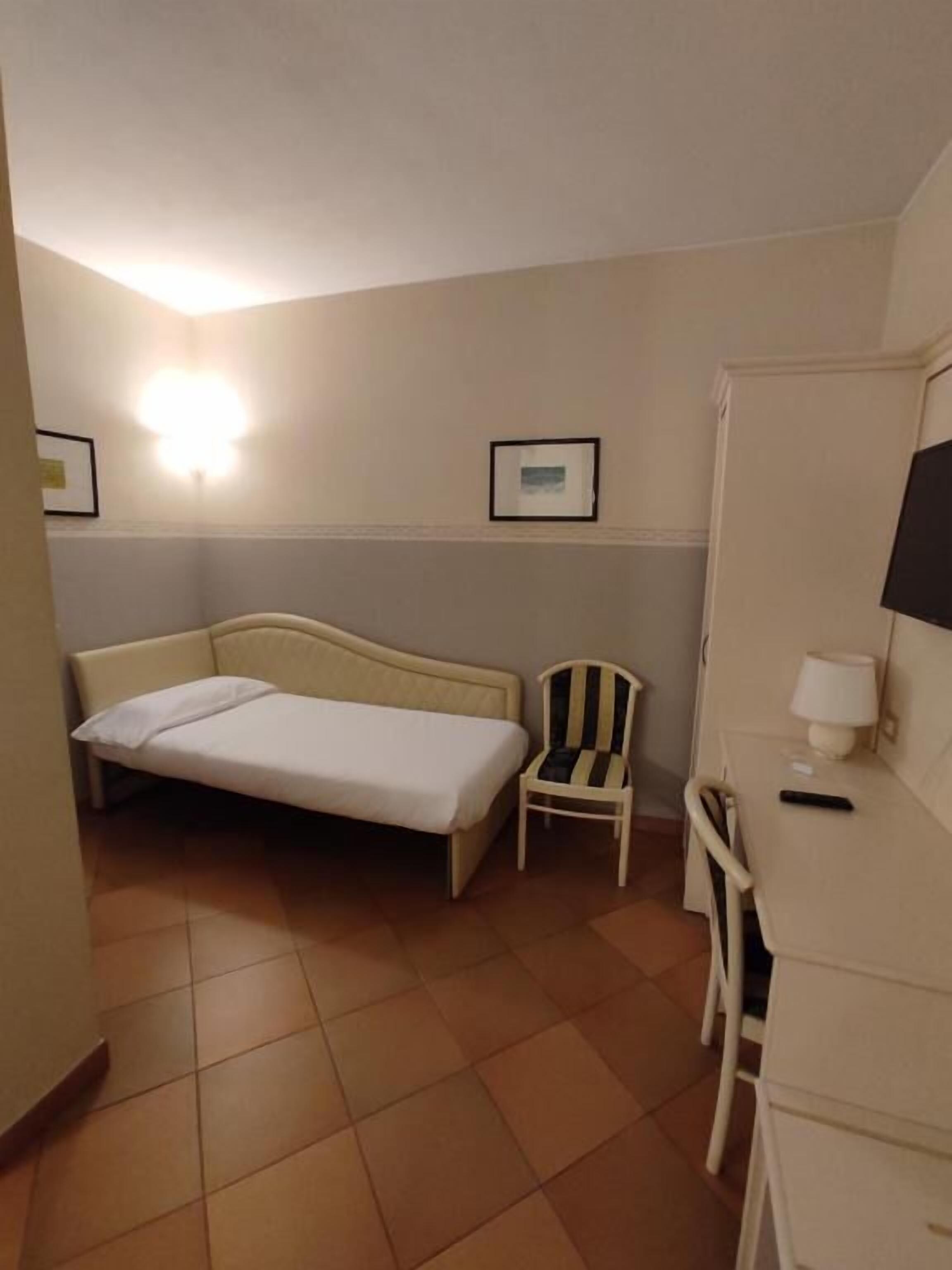 Una habitación pequeña de hotel, con una cama, una silla, un escritorio y un televisor.