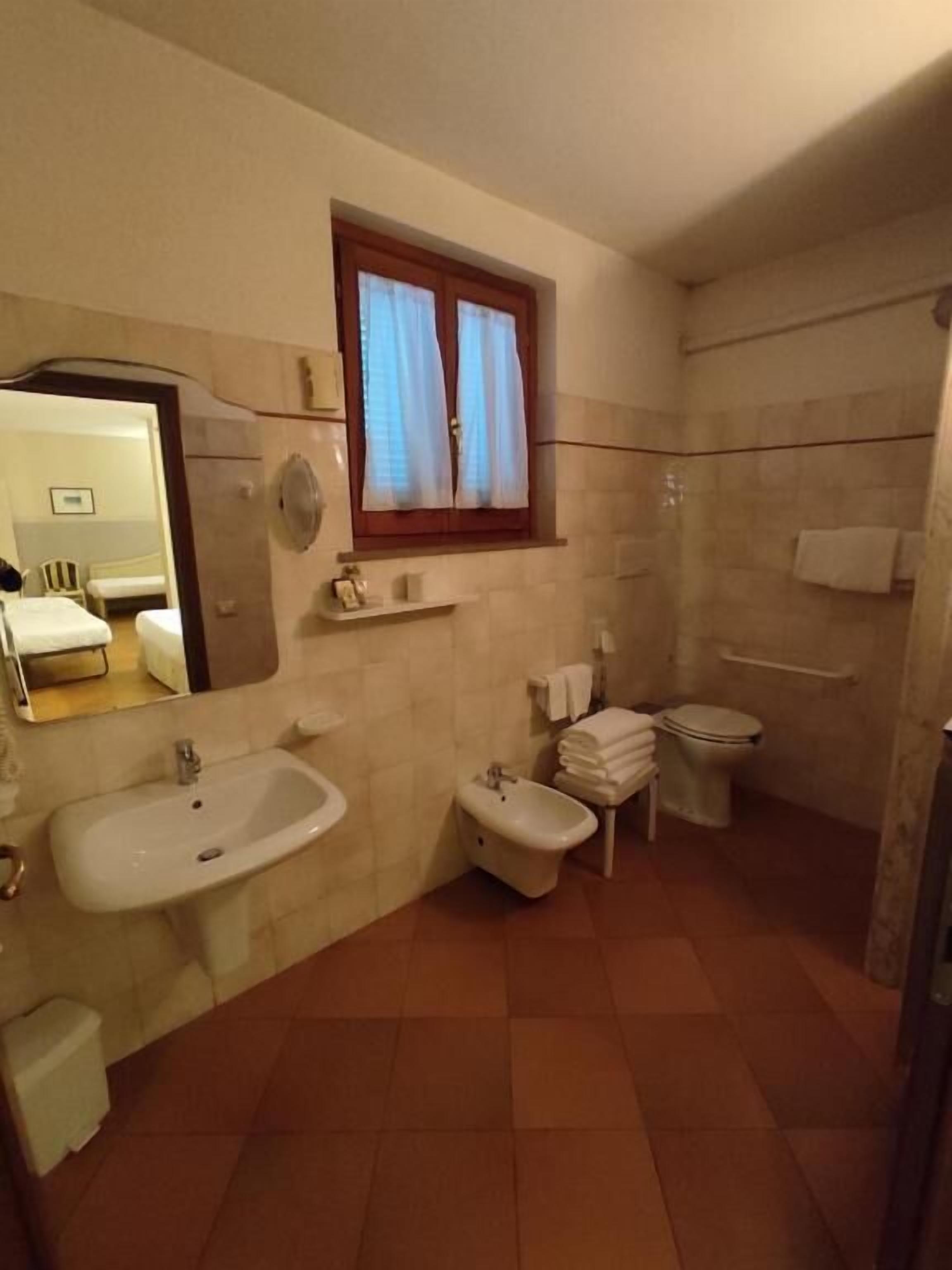 A bathroom with a sink, bidet, toilet, and a window with curtains.