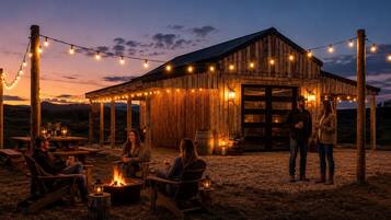A rustic wooden barn with string lights, outdoor seating, and a fire pit.