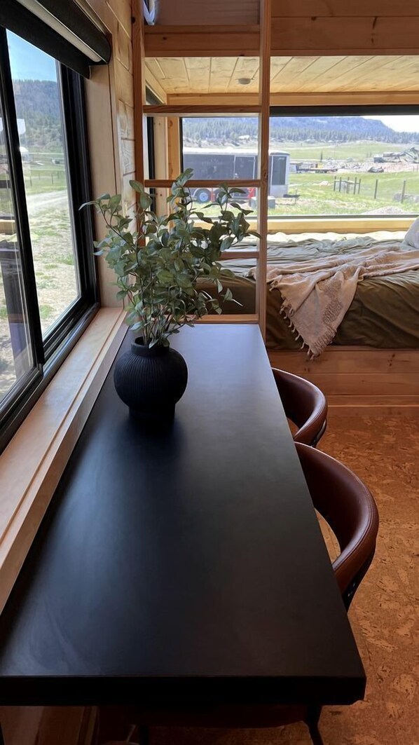 Ein Holzinterieur mit einem Tisch, einer Topfpflanze und einem Bett mit Blick auf eine ländliche Landschaft.