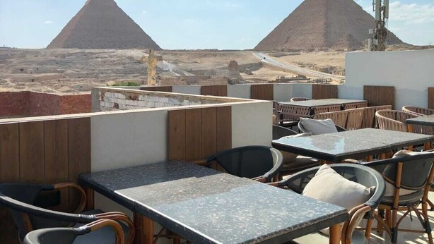 Outdoor seating with tables and chairs, a view of the pyramids, and a clear sky. - Holiday Escape (Giza)