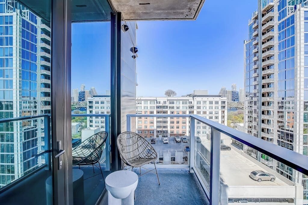Ein Balkon mit zwei Stühlen, einem weißen Tisch und Blick auf einen Parkplatz und Gebäude.