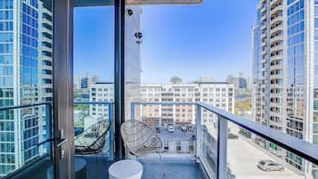 Ein Balkon mit zwei Stühlen, einem weißen Tisch und Blick auf einen Parkplatz und Gebäude.