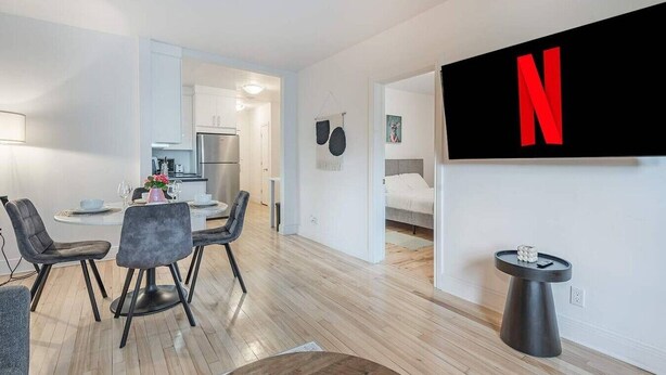 Un apartamento moderno con comedor, cocina y un televisor grande montado en la pared.