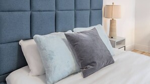 Una cama con cabecera capitonada, una lámpara de noche y dos almohadas.