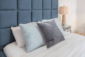 Ein Bett mit einer karrierten Kopfteil, einer Nachttischlampe und zwei Kissen.