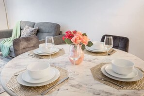 Ein Esstisch ist gedeckt mit weißen Tellern, Schüsseln und Besteck, einer Blumenvase und einer Glasgießer.