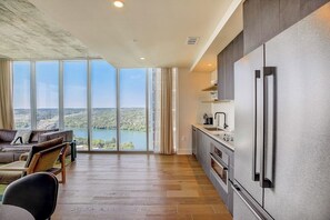 Eine moderne Küche mit einem großen Kühlschrank, ein Essbereich mit Seeblick und eine Sitzecke mit Sofa und Sesseln.