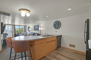 A modern kitchen with a central island, wooden cabinets, a built-in dishwasher, and a wall clock.