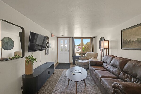 A living room with a sofa, a TV, a coffee table, and a door leading outside.