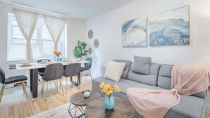 Ein modernes Wohnzimmer mit einem grauen Sofa, einem Esstisch mit Stühlen und zwei abstrakten Bildern an der Wand.
