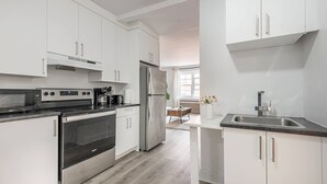 A modern kitchen with white cabinetry, stainless steel appliances, and a central island with a sink. - Spacious Renovated 3BR | Free Parking (Montreal)