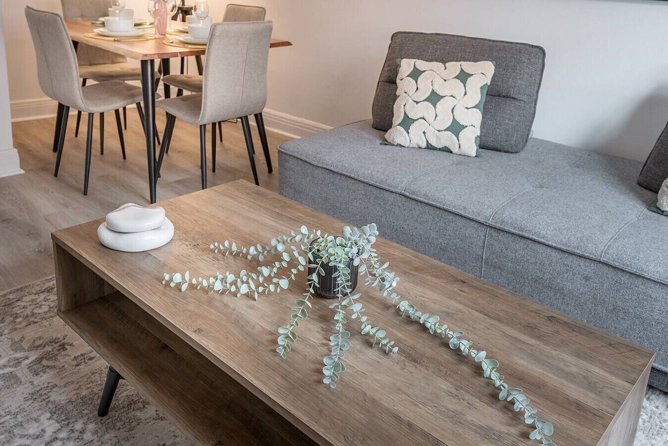 Un salon avec une table basse en bois, un canapé gris et des fauteuils assortis.