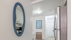 A modern kitchen with white cabinets, a blue-framed mirror, a stainless steel refrigerator, and a framed picture on the wall. - Spacious Renovated 3BR | Free Parking (Montreal)