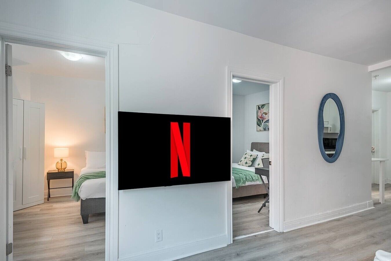 Une chambre d’hôtel moderne dotée d’un grand téléviseur à écran plat fixé au mur, d’un lit recouvert d’une couverture verte, d’une table de chevet avec une lampe et d’un miroir sur le mur.