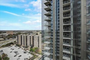 A high-rise building with multiple balconies, a parking lot, and surrounding low-rise buildings. - Stunning Rainey Street condo w/city-view balcony, rooftop pool, gym (Austin)