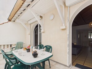 A covered outdoor dining area with a table and chairs, a potted plant, and a door leading to the interior. - Beach 100m away, apartment with terrace for 4 (Longeville-sur-Mer)